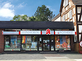 Die Außenansicht der Einhorn Apotheke. Zu sehen ist ein Anbau an ein Fachwerkhaus mit Schaufenster und einem Schild mit dem Namen der Apotheke.
