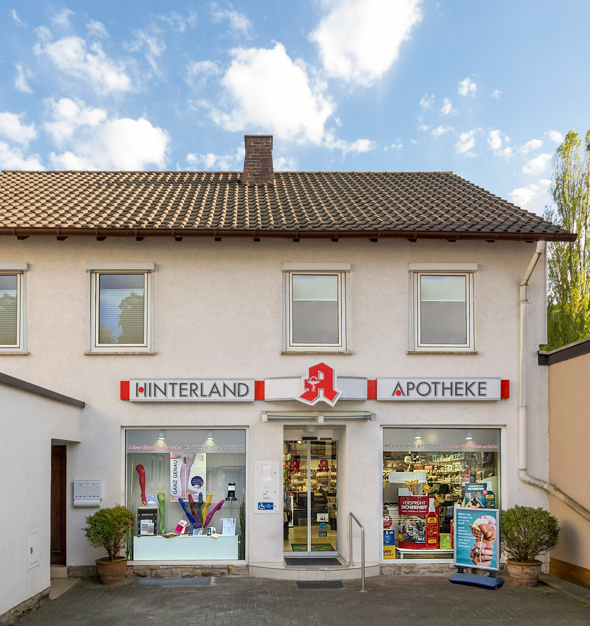 Die Außenansicht der Hinterland-Apotheke. Zu sehen ist eine Hausfront mit Schaufenstern und einem Schild mit dem Namen der Apotheke.
